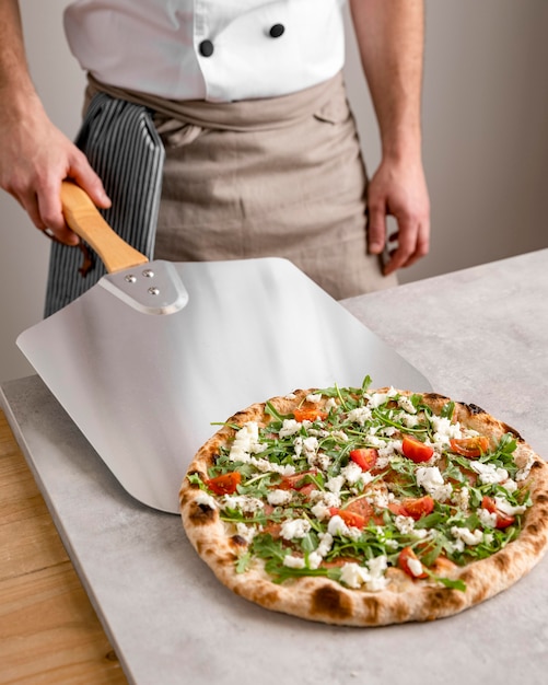 Foto hombre de alto ángulo agarrando pizza con herramienta de cáscara