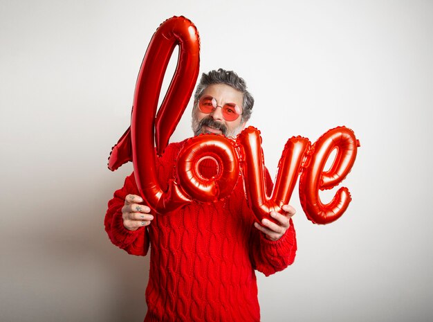 Hombre amable con gafas sosteniendo un globo rojo con la palabra amor sobre fondo blanco.