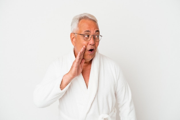 Hombre americano senior con bata de baño aislado sobre fondo blanco está diciendo una noticia secreta de frenado en caliente y mirando a un lado