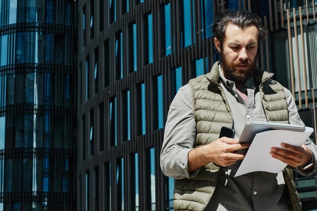Hombre analizando documentos fuera de un edificio de oficinas moderno