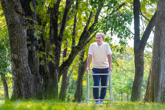 Hombre anciano asiático con caminador caminando solo en el parque disfrutando de la hermosa naturaleza y la vida silvestre durante el verano para ejercicio ligero y fisioterapia después de un programa de recuperación de cirugía de rodilla