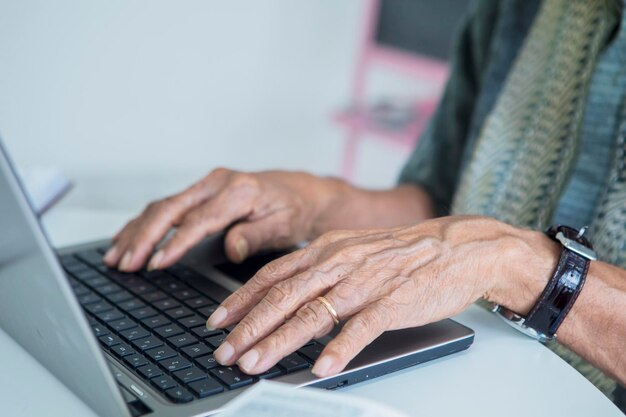 Hombre anciano con las manos trabajando con una computadora portátil en la mesa