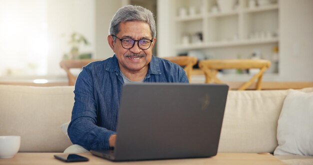 Foto hombre anciano y sonrisa para portátil sala de estar en el sofá para escribir correo electrónico o mensaje para la comunicación persona mayor mirando la pantalla y gafas con tecnología internet o web para trabajar desde casa