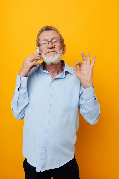 Hombre anciano con teléfono posando sobre fondo amarillo