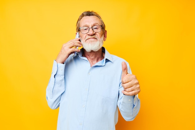 Hombre anciano con teléfono posando sobre fondo amarillo