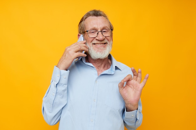 Hombre anciano con teléfono posando sobre fondo amarillo