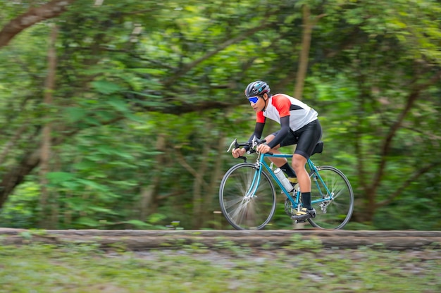 Un hombre anda en bicicleta por la carretera. Hombre montando bicicleta deportiva vintage para hacer ejercicio por la noche. Un hombre en bicicleta para respirar el aire fresco en medio de la naturaleza, pradera, bosque, con el sol vespertino brillando a través de