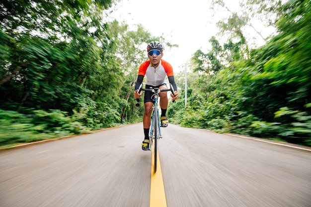 Un hombre anda en bicicleta por la carretera. Hombre montando bicicleta deportiva vintage para hacer ejercicio por la noche. Un hombre en bicicleta para respirar el aire fresco en medio de la naturaleza, pradera, bosque, con el sol vespertino brillando a través de