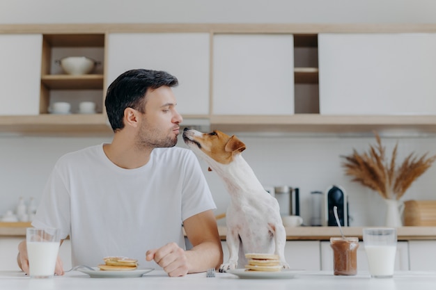 Hombre anfitrión besa con perro, come deliciosos panqueques