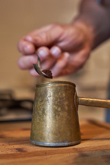 Hombre anónimo de cultivo que vierte café aromático en cezve de metal colocado en una mesa de madera mientras cocina el desayuno