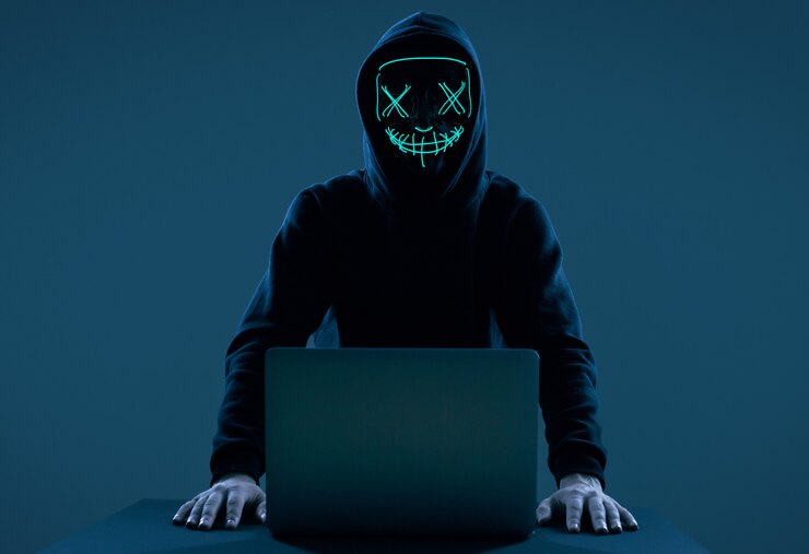 Foto hombre anónimo con una sudadera negra y una máscara de neón hackeando una computadora