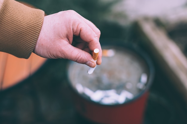 Un hombre apaga un cigarrillo en la basura.