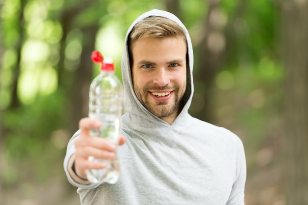 El hombre con apariencia atlética sostiene una botella con agua. Atleta hombre en ropa deportiva entrenando al aire libre. Concepto de deporte y estilo de vida saludable. Atleta bebe agua después del entrenamiento, fondo de naturaleza.