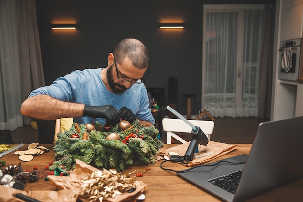 Hombre aprendiendo a decorar una corona de Navidad viendo la lección en línea