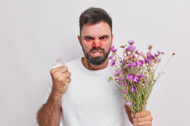 El hombre aprieta el puño y los dientes se ve indignado. Sufre de alergia estacional. Tiene enrojecimiento de la nariz y los ojos hinchados. Tiene una servilleta alérgica a las flores silvestres. Problemas de salud