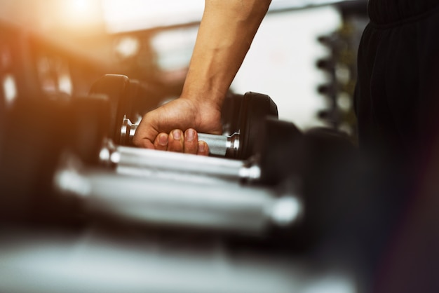 Hombre de la aptitud en el entrenamiento que muestra ejercicios con pesas de gimnasia en gimnasio