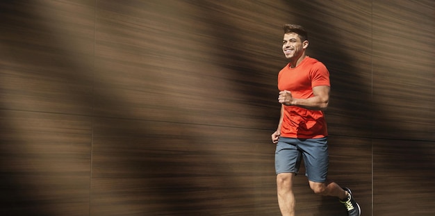 Hombre apto feliz corriendo al aire libre por la mañana al lado de fondo de madera, espacio libre, panorama