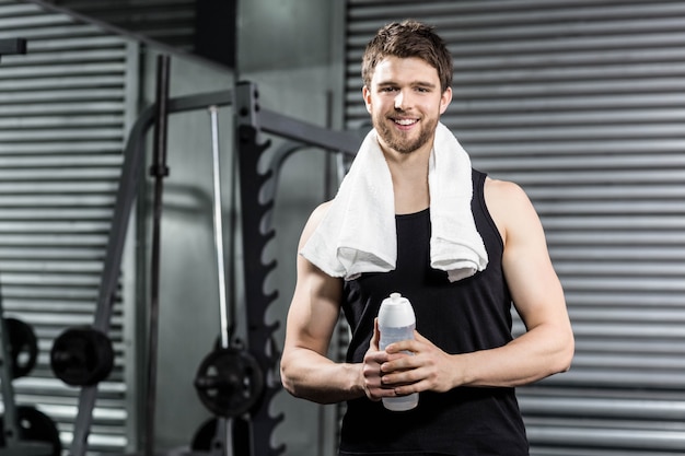 Hombre apto que sostiene la botella de agua en el gimnasio de crossfit