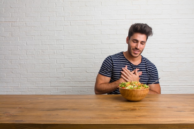 Hombre apuesto y natural joven sentado en una mesa haciendo un gesto romántico