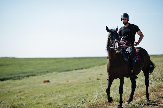 Un hombre árabe con barba alta usa casco negro, monta un caballo árabe.