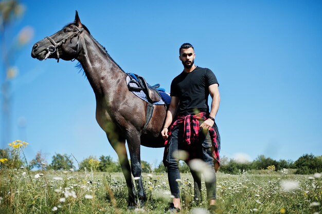 Hombre árabe de barba alta vestido de negro con caballo árabe.