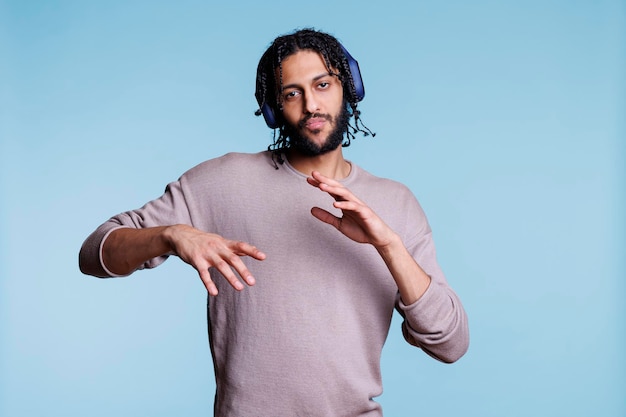 Hombre árabe confiado haciendo movimientos geniales mientras escucha música en auriculares y mira la cámara. Joven bailando mientras disfruta de la lista de reproducción de canciones en el retrato de los auriculares