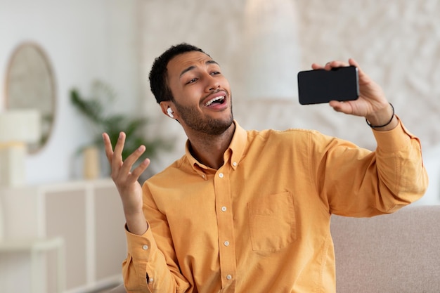 Hombre árabe feliz usando teléfono celular con auriculares y cantando