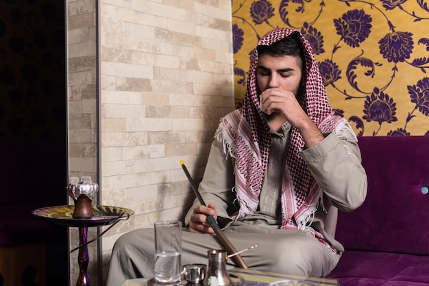 Hombre árabe fumando shisha y bebiendo café