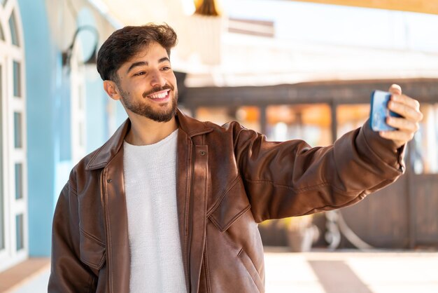 Un hombre árabe guapo al aire libre haciendo un selfie con un teléfono móvil