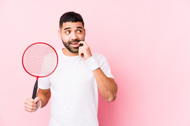 El hombre árabe joven que jugaba a bádminton aisló relajado pensando en algo que miraba un espacio de la copia.