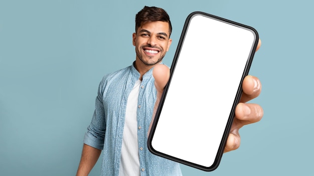 Hombre árabe joven que muestra el teléfono con pantalla en blanco