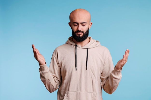 Hombre árabe rezando a dios con las manos abiertas y los ojos cerrados, suplicando bendición y perdón. Joven espiritual alabando y suplicando por la paz con gesto de brazos levantados