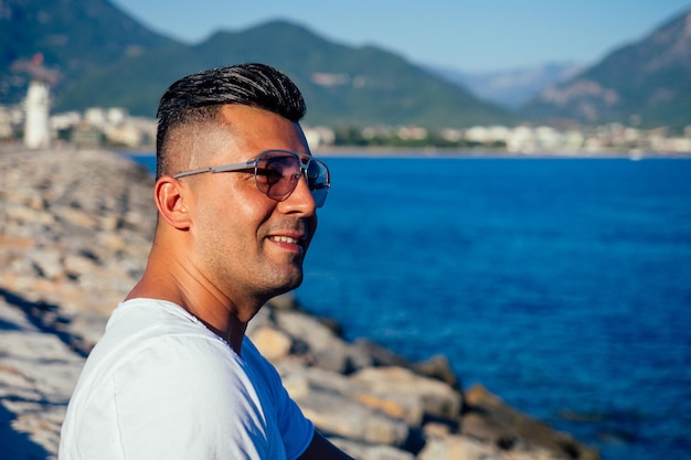 Hombre árabe rico en moda usa gafas de sol y tshort blanco posado contra el mar arábigo