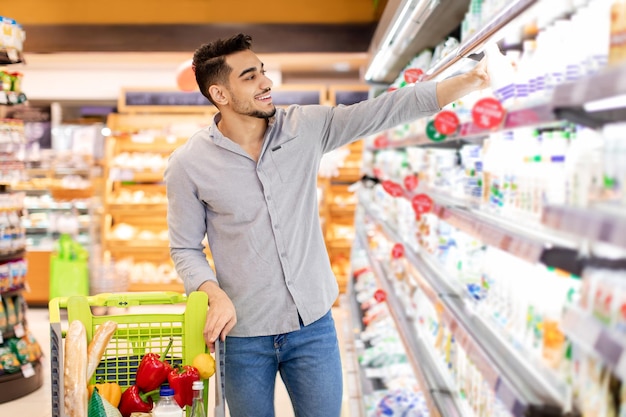 Hombre árabe tomando una botella de leche comprando comestibles en el supermercado