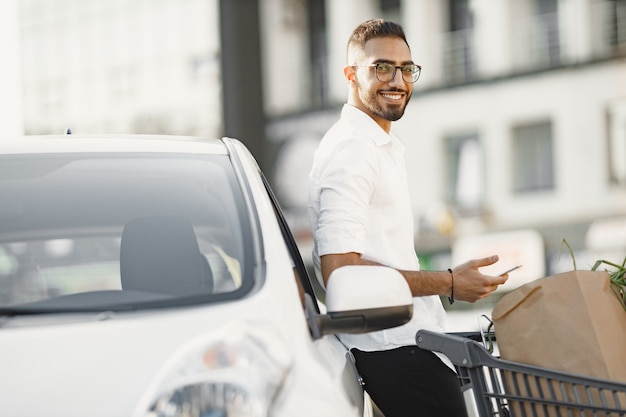 El hombre árabe usa un teléfono inteligente mientras espera cargar la batería en el automóvil.