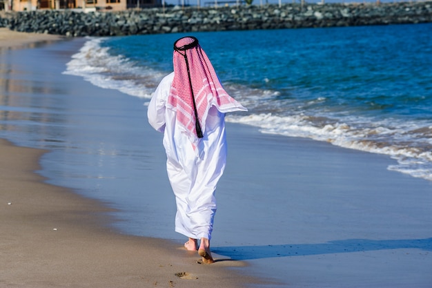 El hombre árabe vestido de Oriente Medio posa delante de la costa del mar.