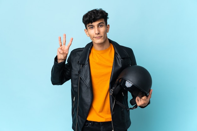 Hombre argentino con un casco de moto feliz y contando tres con los dedos