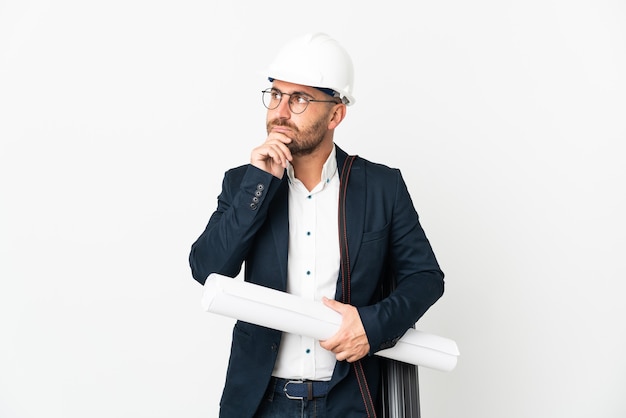 Hombre arquitecto con casco y sosteniendo planos aislados en blanco con dudas