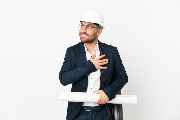 Hombre arquitecto con casco y sosteniendo planos aislados en la pared blanca mirando hacia arriba mientras sonríe