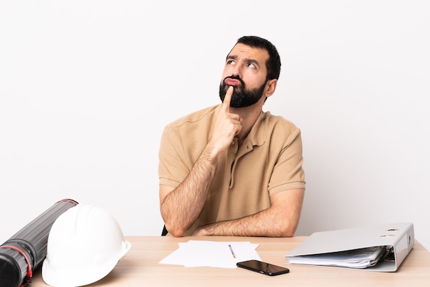 Foto hombre de arquitecto caucásico con barba en una mesa con dudas mientras mira hacia arriba.