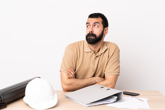 Hombre de arquitecto caucásico con barba en una mesa con dudas mientras mira hacia arriba