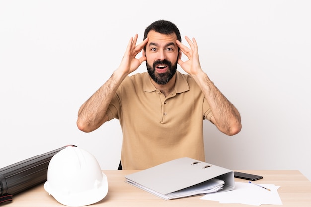 Hombre de arquitecto caucásico con barba en una mesa con expresión de sorpresa