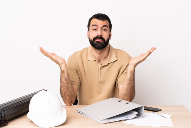 Hombre de arquitecto caucásico con barba en una mesa haciendo gesto de dudas