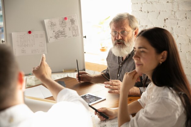 Hombre arquitecto-ingeniero presenta proyecto de futura casa para familia joven. Hombre que trabaja en la oficina con documentos, planos. Primera casa, industrial, concepto de construcción. Mudarse a un nuevo lugar para vivir.