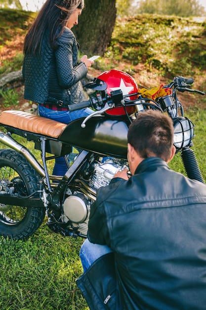 Foto hombre arreglando su moto mientras su novia mira el móvil