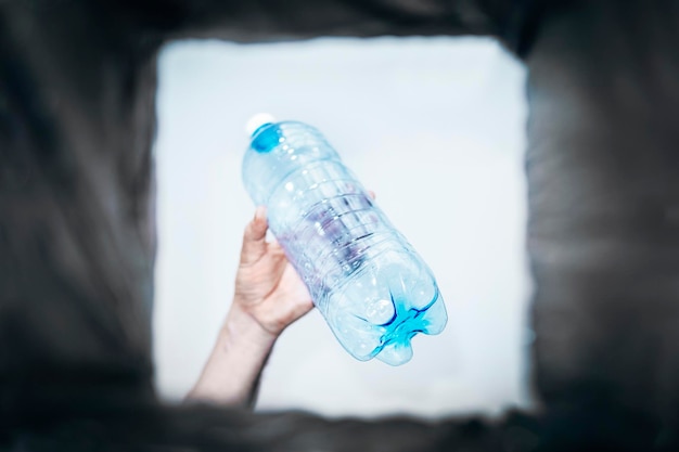 El hombre arroja una botella de plástico vacía a un bote de basura Vista inferior del bote de basura El problema del reciclaje y la contaminación del planeta con basura