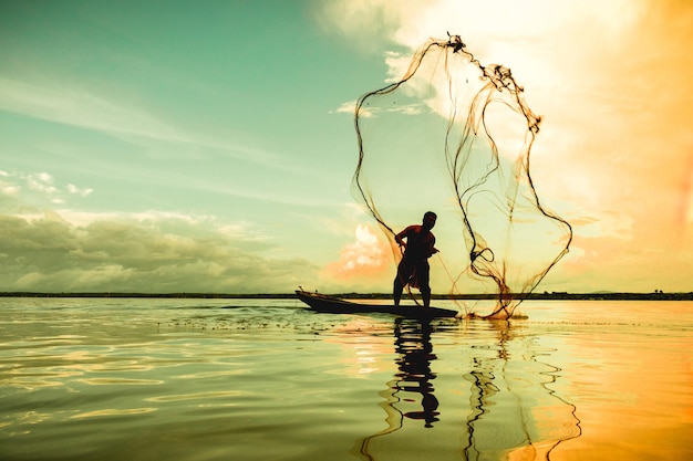 Hombre arrojando una red de pesca en el lago contra el cielo durante la puesta del sol