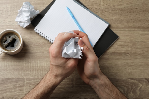 Hombre arrugando papel sobre tabla de madera con cuaderno y taza de café, vista superior