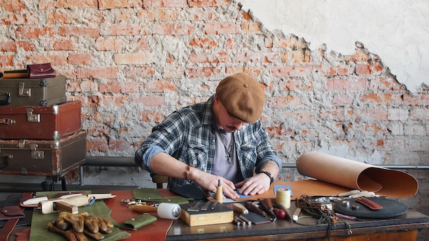 Hombre artesano de cuero cose una billetera de cuero en el taller. Fabricación de productos de cuero hechos a mano.