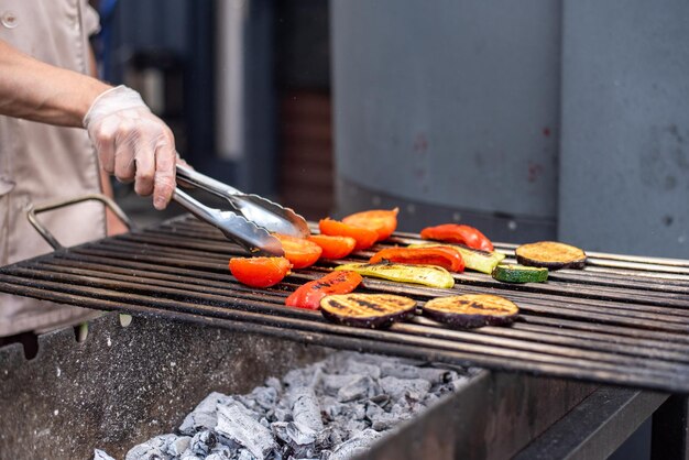 Un hombre asa verduras en una parrilla con carbones